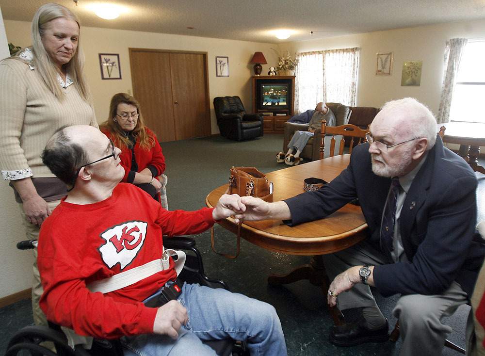 Ron Stevens, right, knows his son doesn't recognize him, but Jim responds positively to the loving touch of a once-familiar hand. Looking on are Sheltered Living employees Dianna Mitchell and Trish Schomacker.